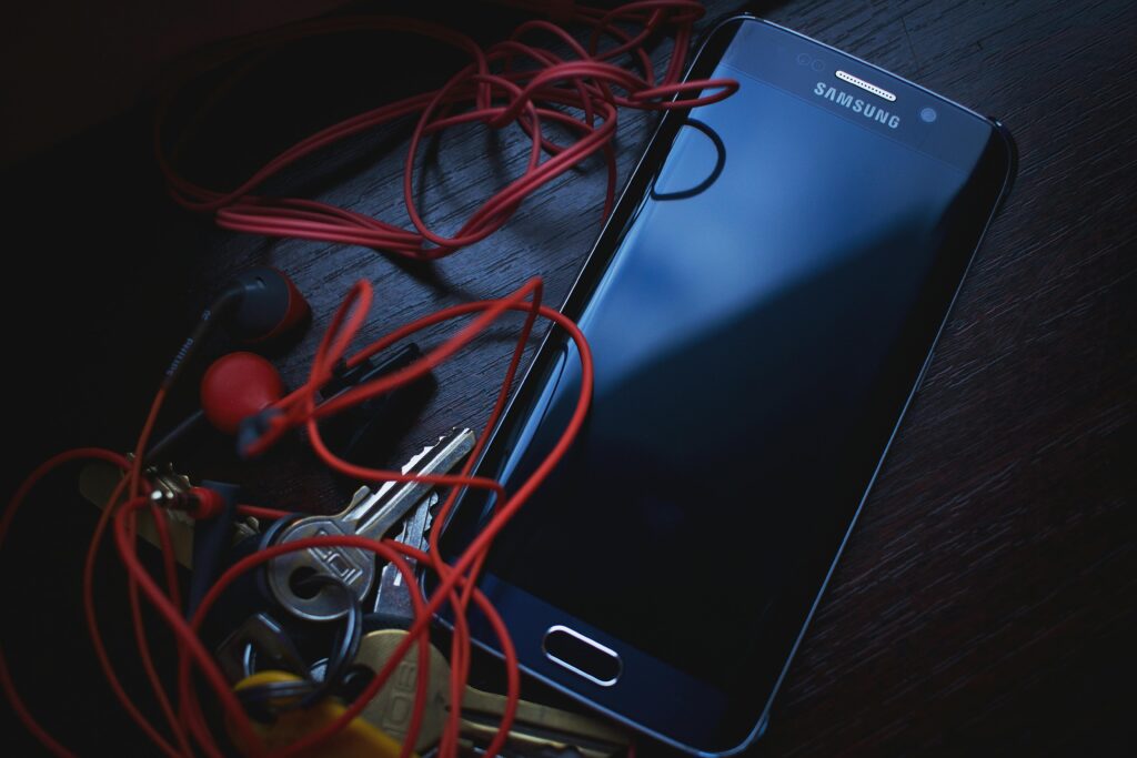 Samsung smartphone with red earbuds and keys on a wooden table, in natural lighting.